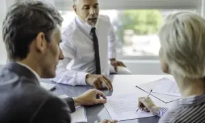 Trzy osoby przy stole omawiają dokumenty. Kobieta podpisuje umowę, co może sugerować, że banki pracują w sobotę.