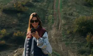 Kobieta z telefonem na tle pagórkowatego krajobrazu, idealnego do **roaming Wielka Brytania**.