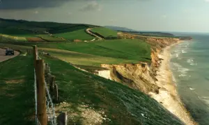 Malownicze klify i plaża na wyspie Wight, z krętą drogą i zielonymi wzgórzami w tle.