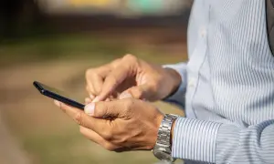 Mężczyzna w koszuli z paskami używa smartfona, szukając informacji, jak zamknąć konto Revolut.