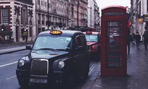 Czarne taksówki i czerwona budka telefoniczna na ulicy w Londynie.