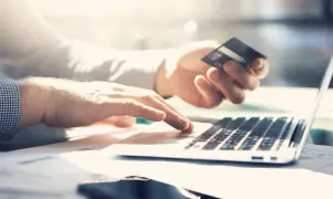 Dłonie wpisują dane karty na laptopie, planując płatność za granicą. Sprawdź prowizję za płatność kartą za granicą PKO BP.