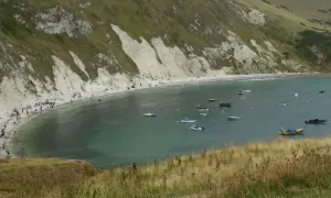 Malownicze morze w Anglii, zatoka pełna łodzi, z plażą i ludźmi w oddali.