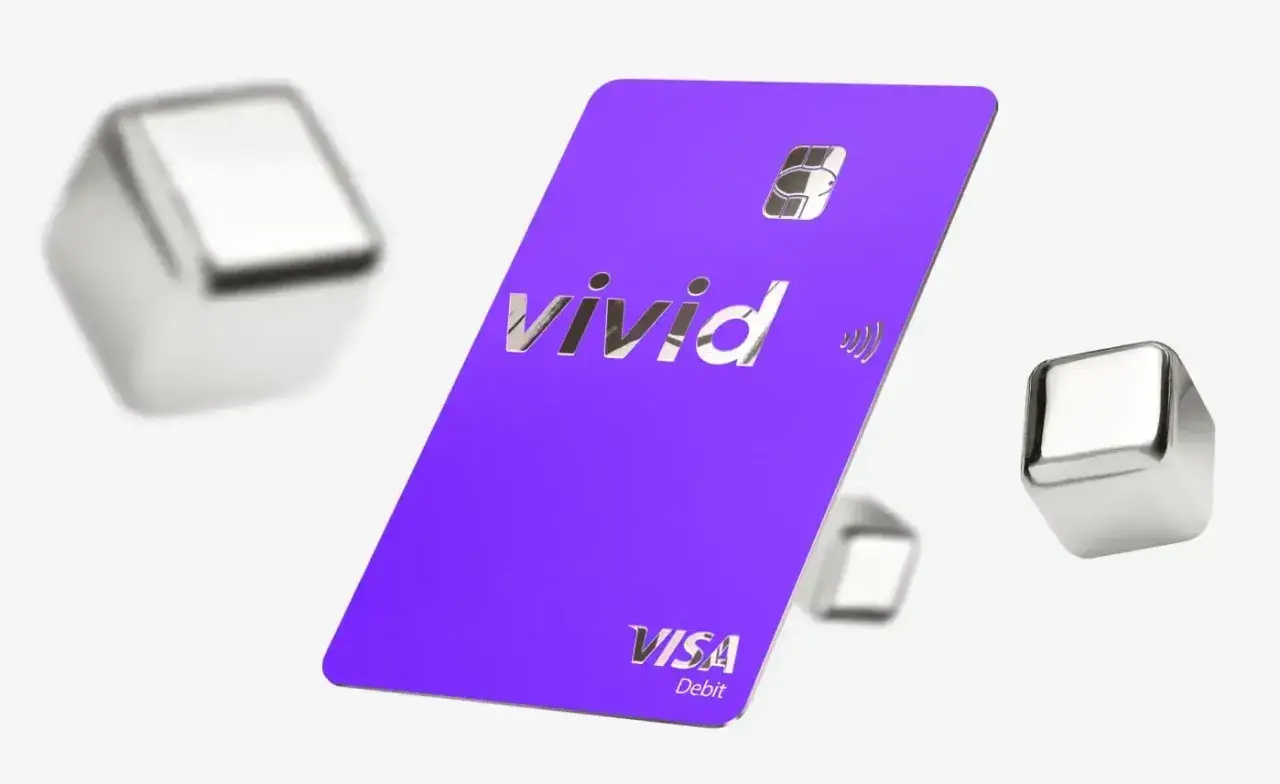 Fioletowa karta płatnicza Vivid Visa Debit, otoczona metalicznymi sześcianami, symbolizuje dostęp do żywych pieniędzy i nowoczesnych płatności.