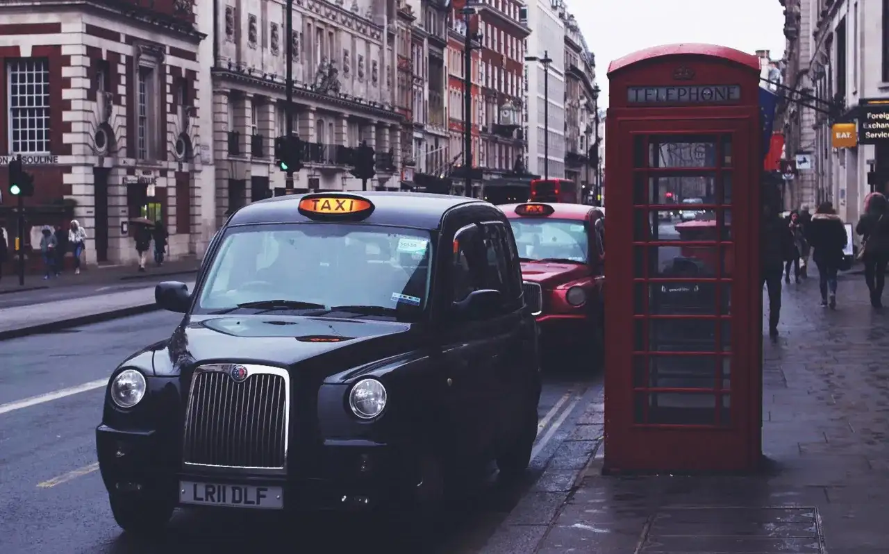 Czarne taksówki i czerwona budka telefoniczna na ulicy w Londynie.