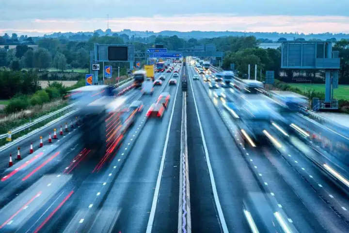 Autostrada w Wielkiej Brytanii, ruchliwy dzień. Wiele samochodów i ciężarówek w ruchu, tworząc smugi światła.